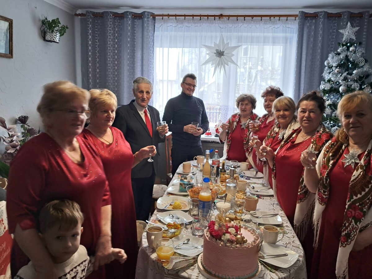 Cały zespół Jargocianie, Marek Szulikowski są na uroczystym obiedzie. Zespół odwiedził Władzię z okazji jej urodzin. Wszyscy stoją w okół stoła.