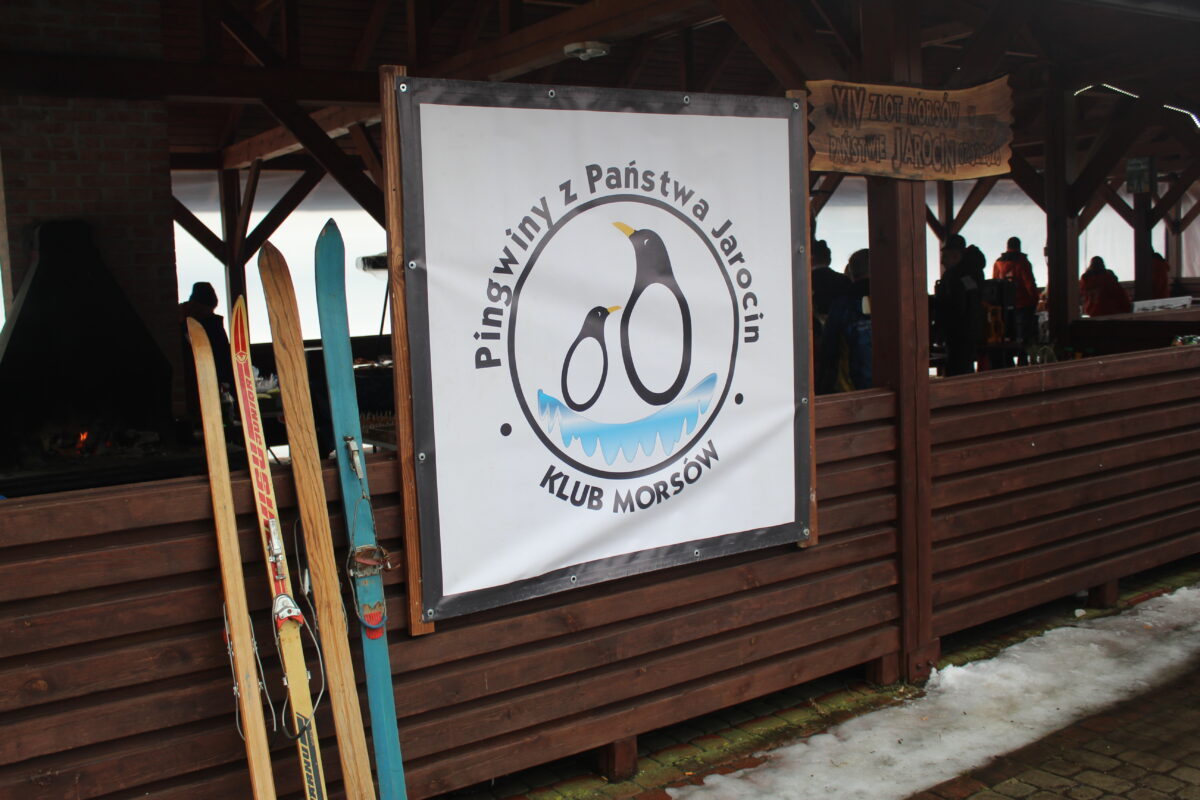 Wypożyczalnia nart przy logo Klubu Morsów Pingwiny z Państwa Jarocin i deske z napisem XIV Zlot morsów w państwie Jarocin 07.02.2026