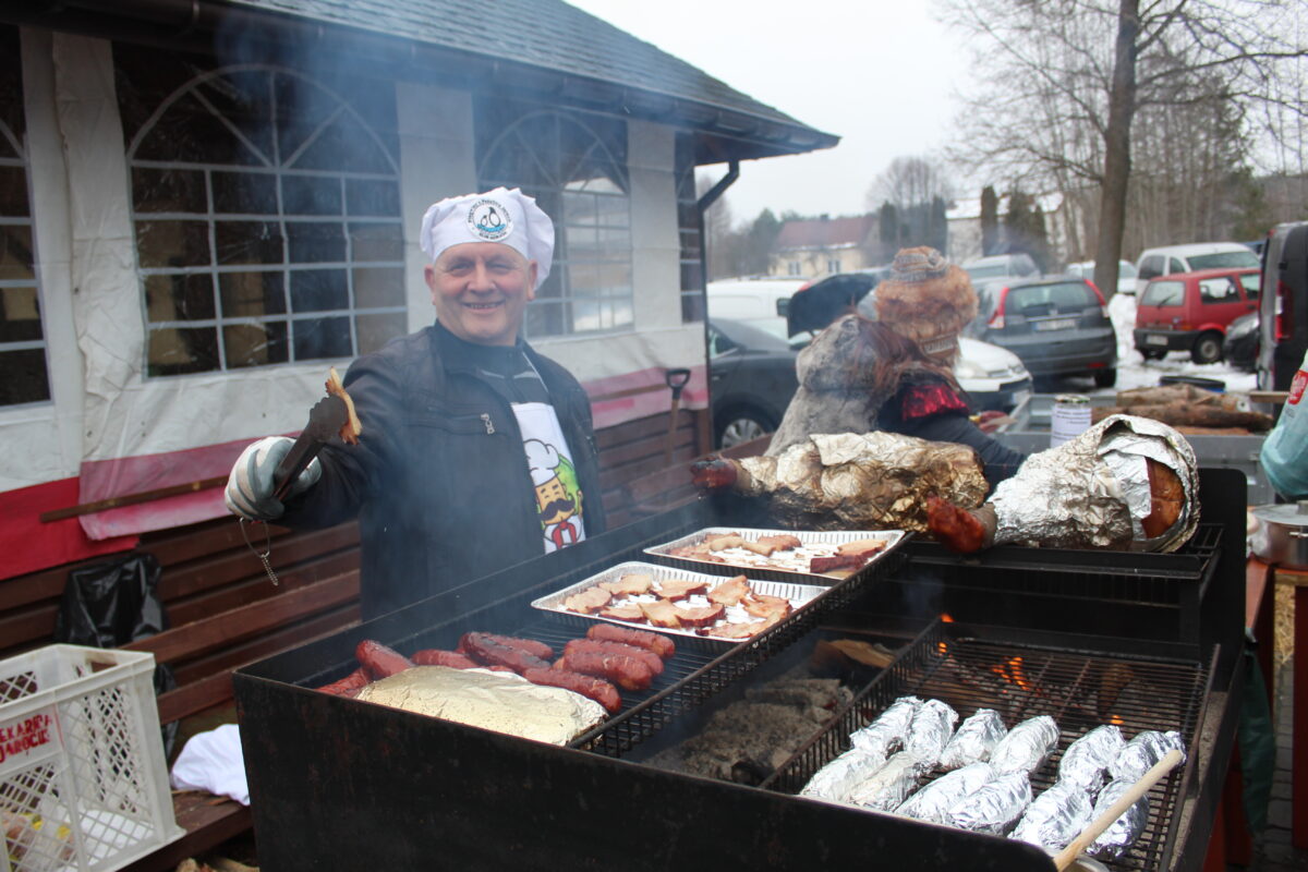 Pan częstuje boczkiem i kiełbasą którą smaży na grilu