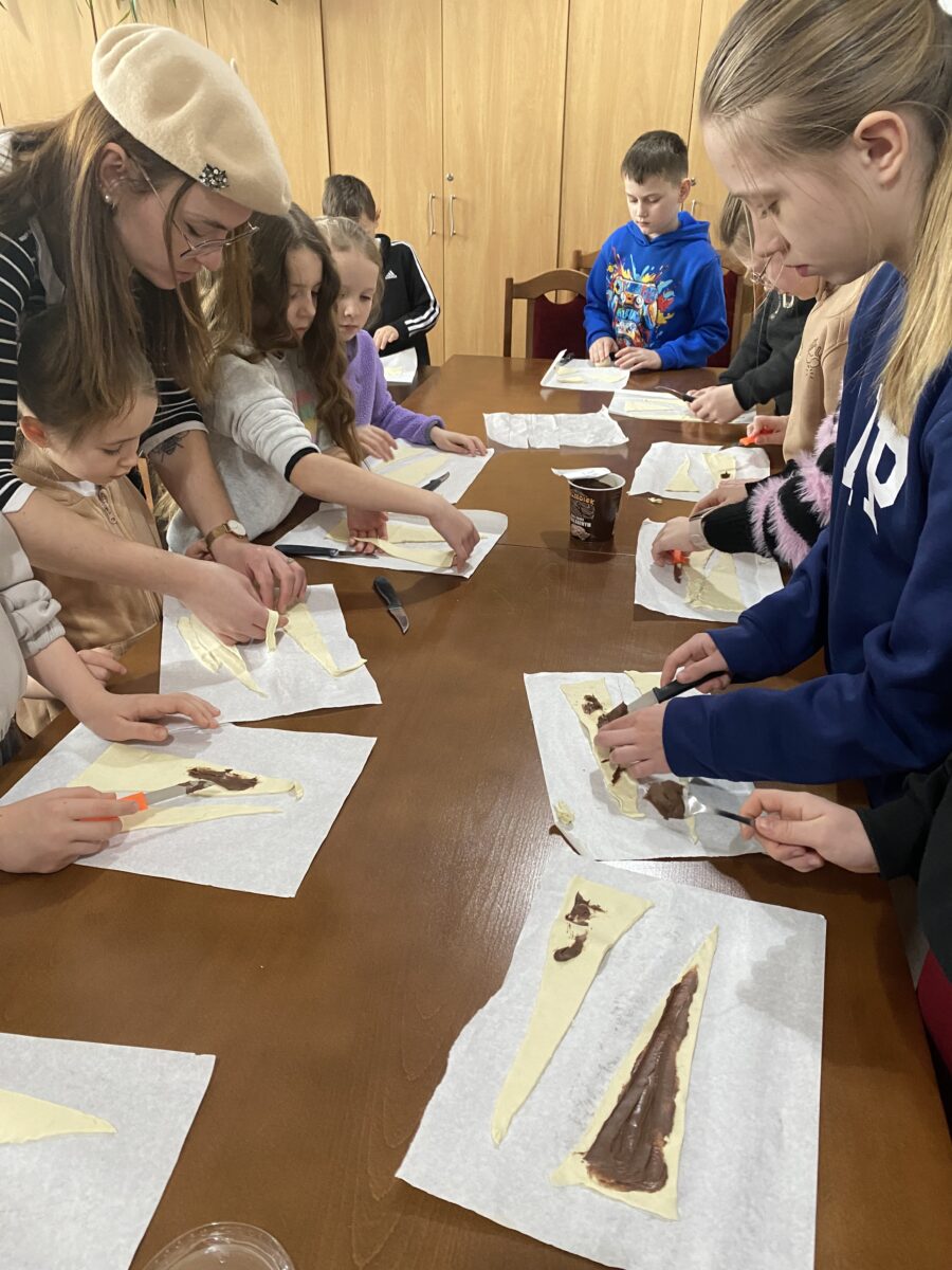 Dziewczyny smarują ciasto francuskie z czekoladą, pani Iza też pomaga