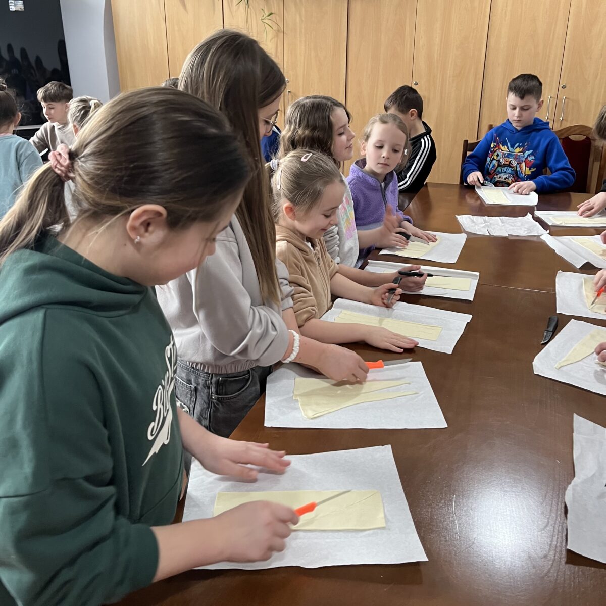 Widać dziewczyny które zaczynają kroić ciasto francuzkie, Lena patrzy na koleżankę jak robi