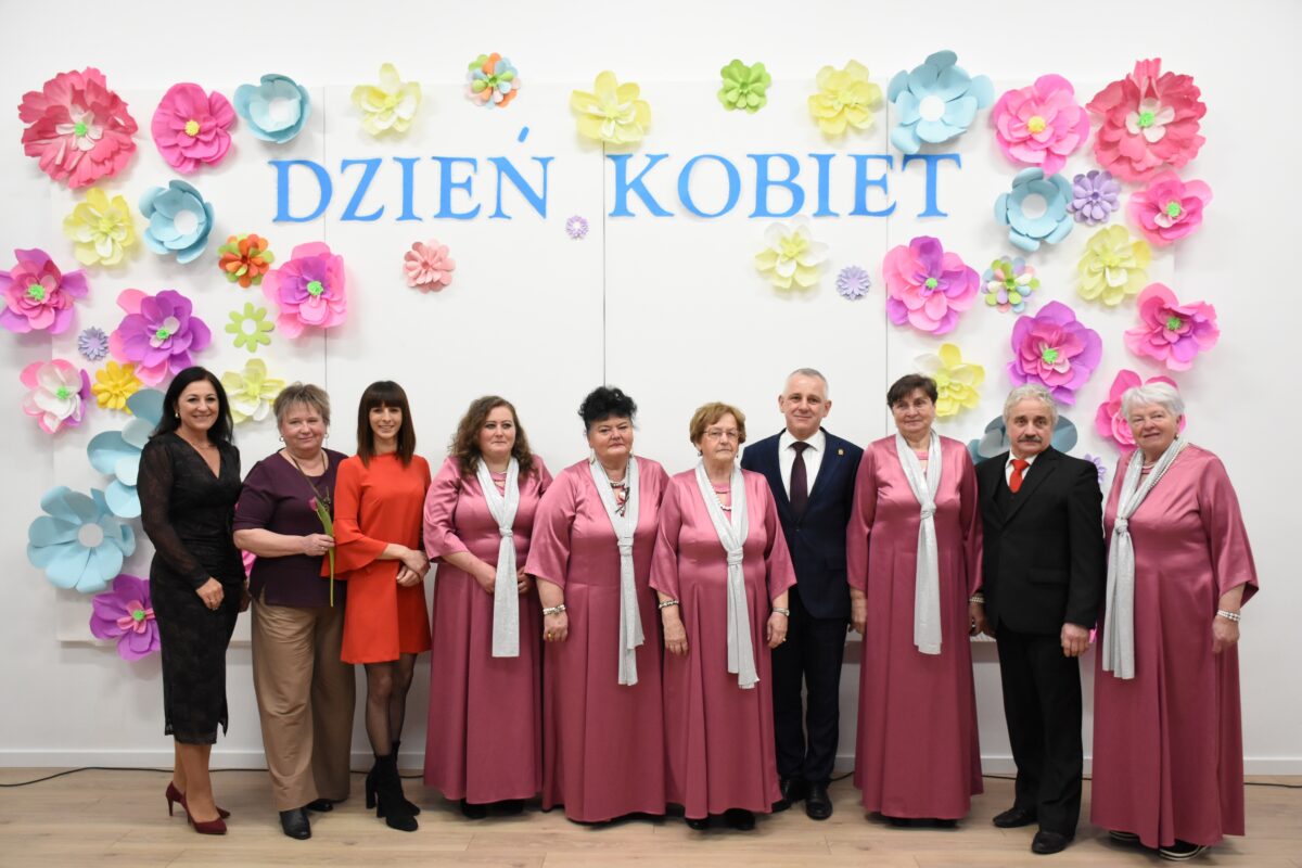 Brokaty, radni i pan Wójt pozują przed ścianką na Dnia Kobiet