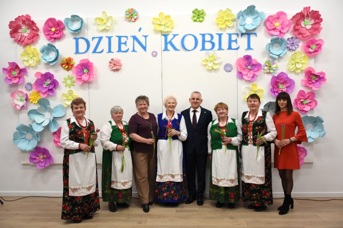 Wesołe Kumosie radni i pan Wójt pozują przed ścianką na Dnia Kobiet