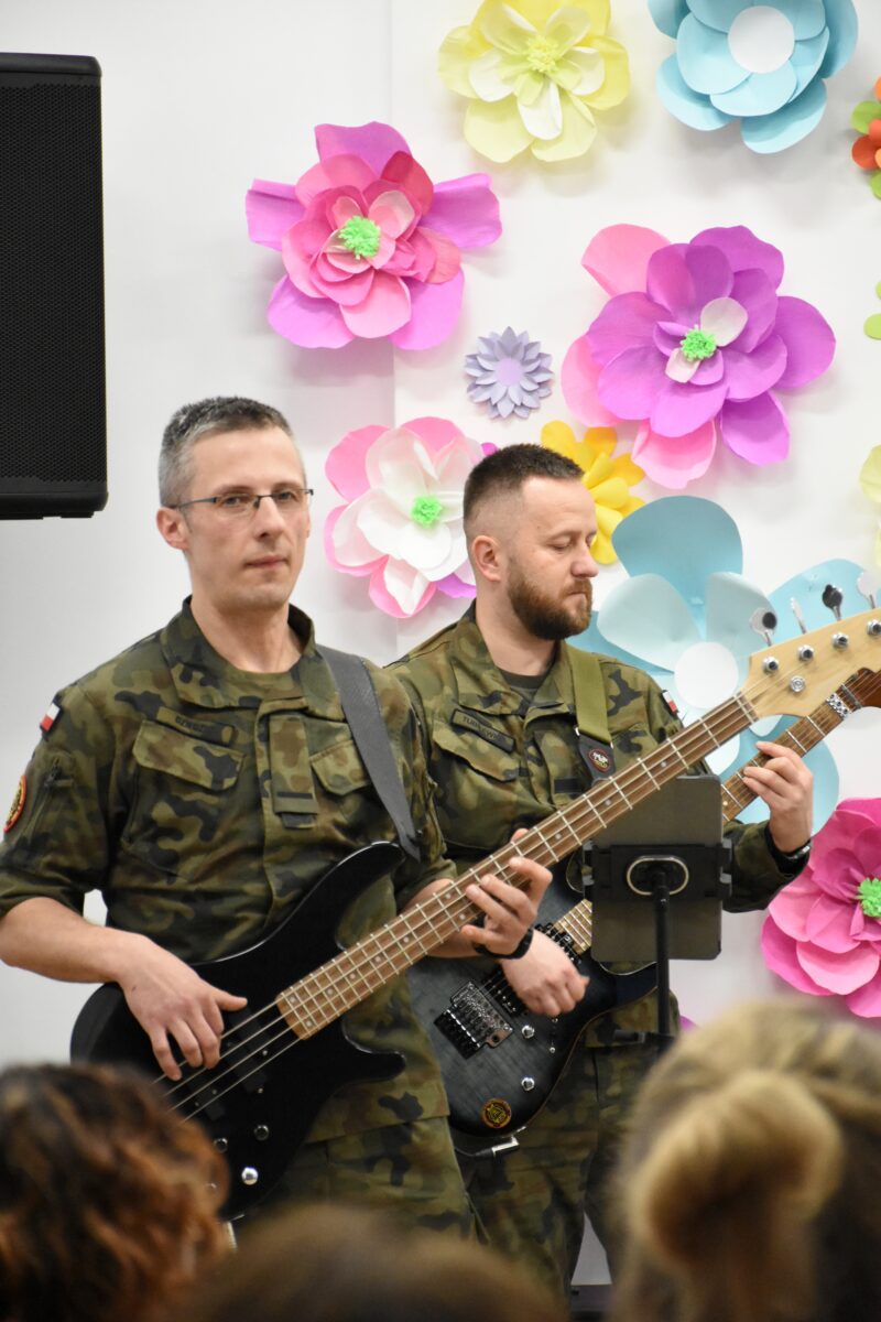 Zbliżenie na basiste i gitarzysta z zespołu Saper Band, i na tle kwiaty ścianki