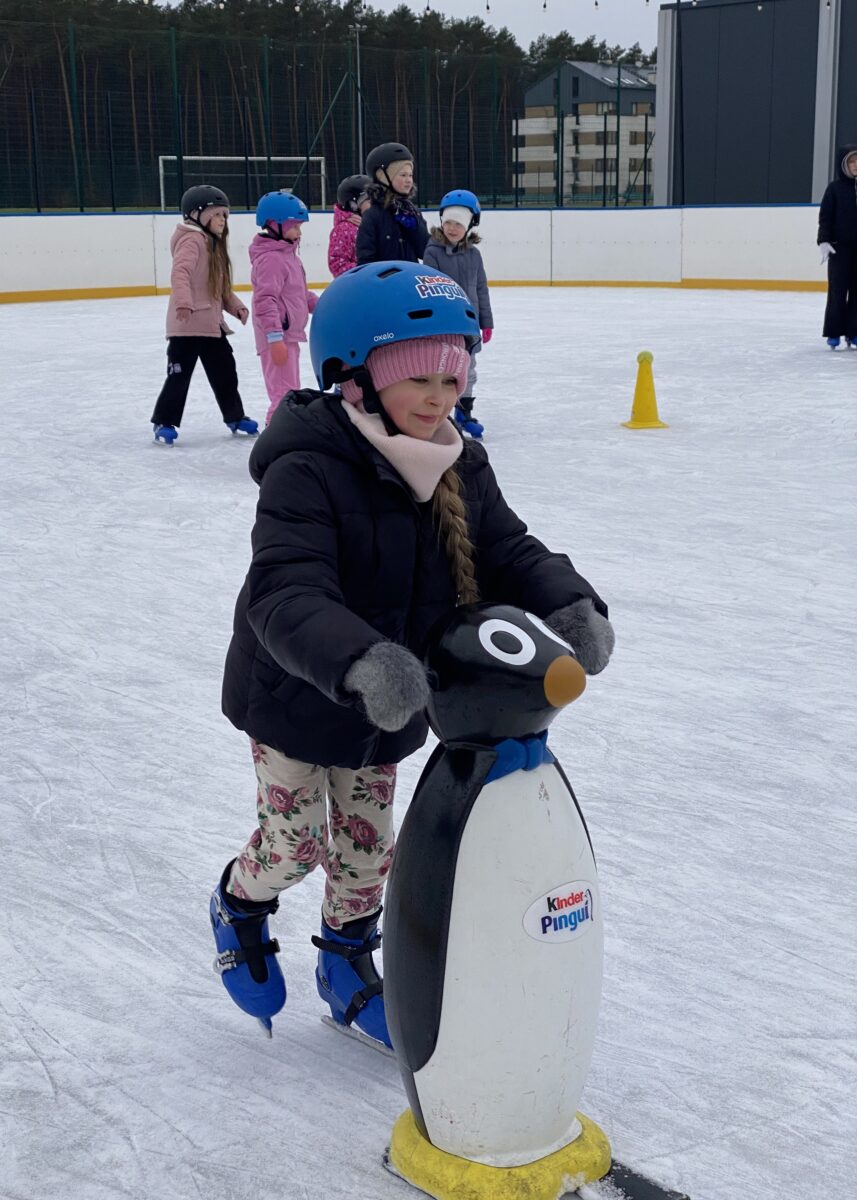 Justyna z uśmiechem pcha pingwina na łyżwach