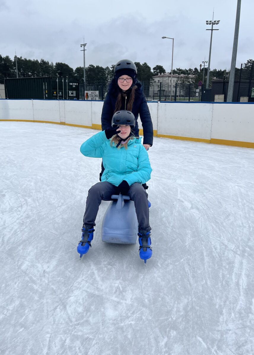 Sara siedzi na wieloryb gdzie Sandra go pcha na łyżwach. Oby dwie z uśmiechem