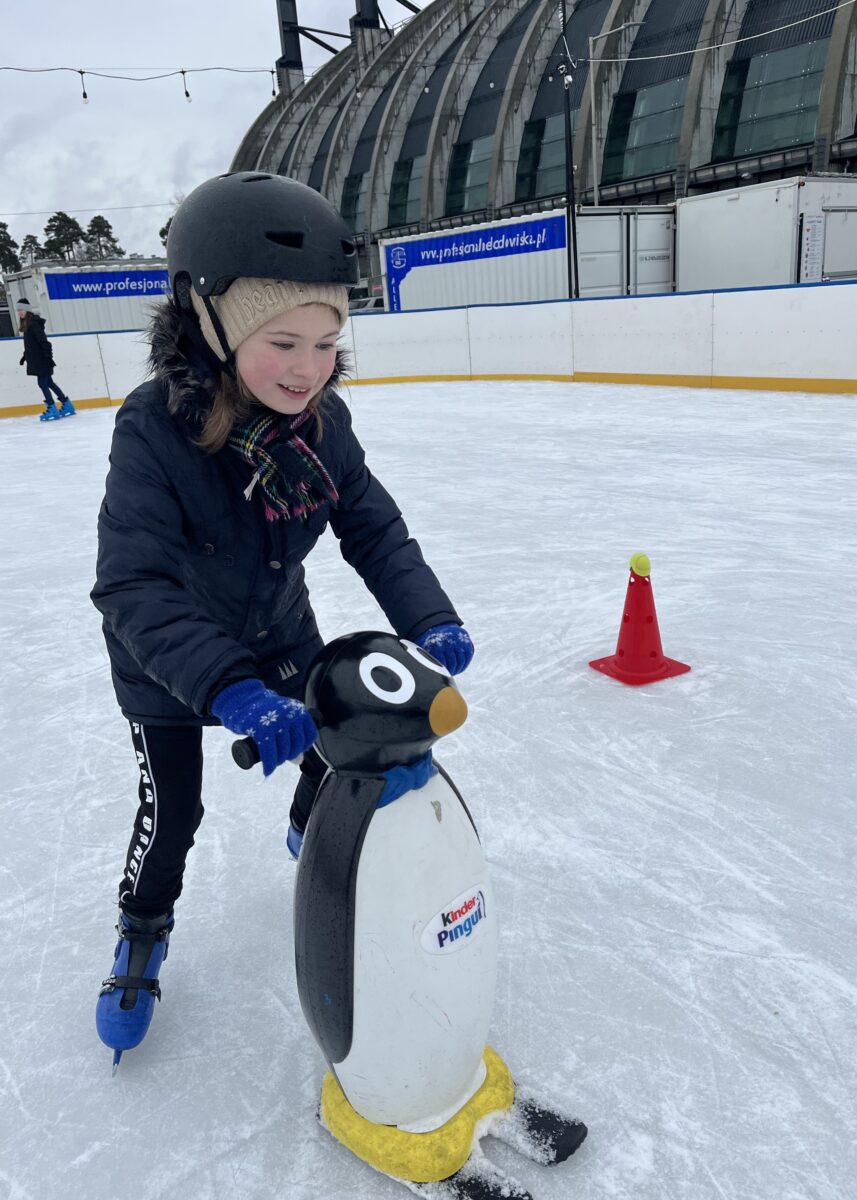 Maja z uśmiechem pcha pingwina na łyżwach