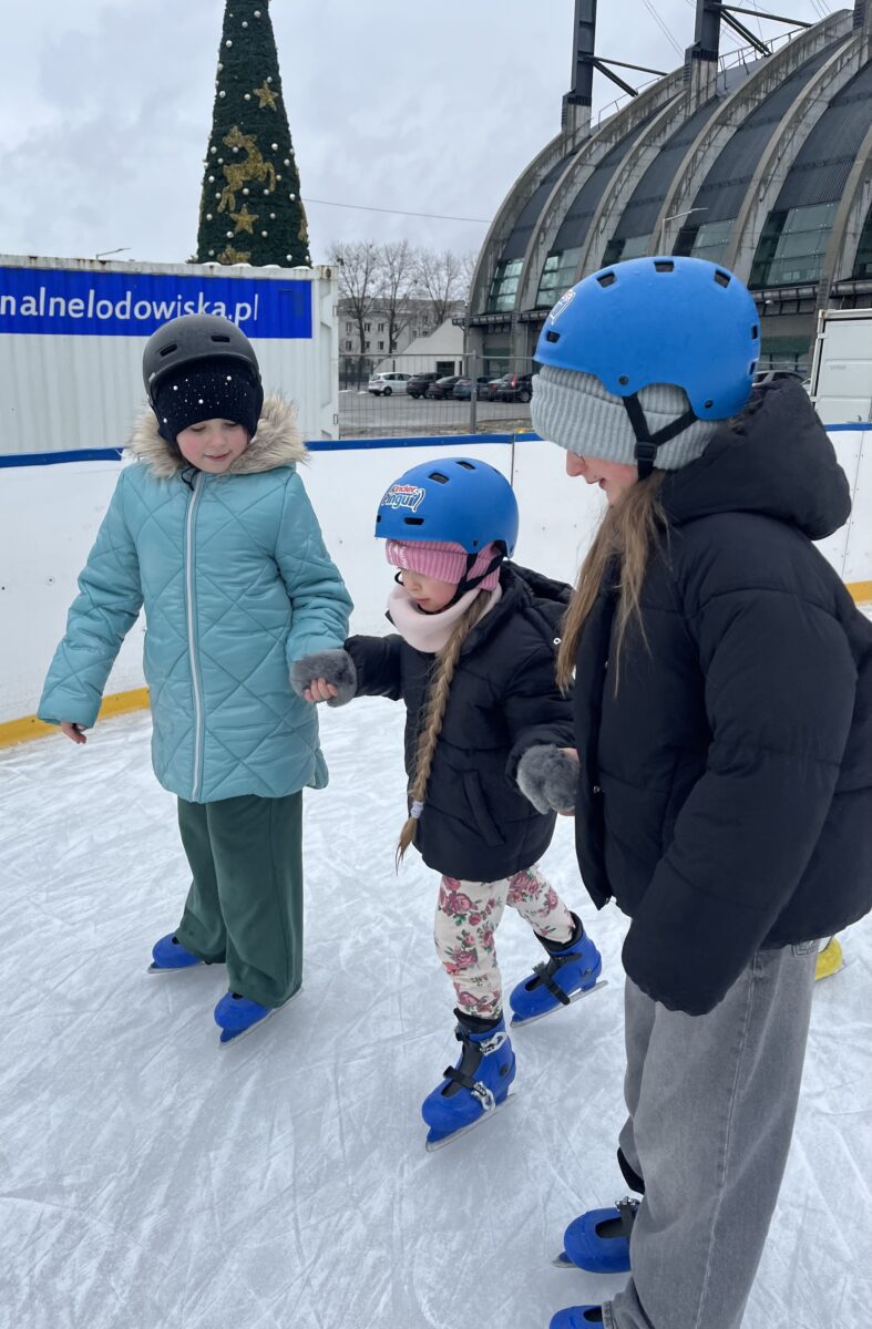 Marysia i Natalia trzymają rękę Justynki jeżdżąc na łyżwach