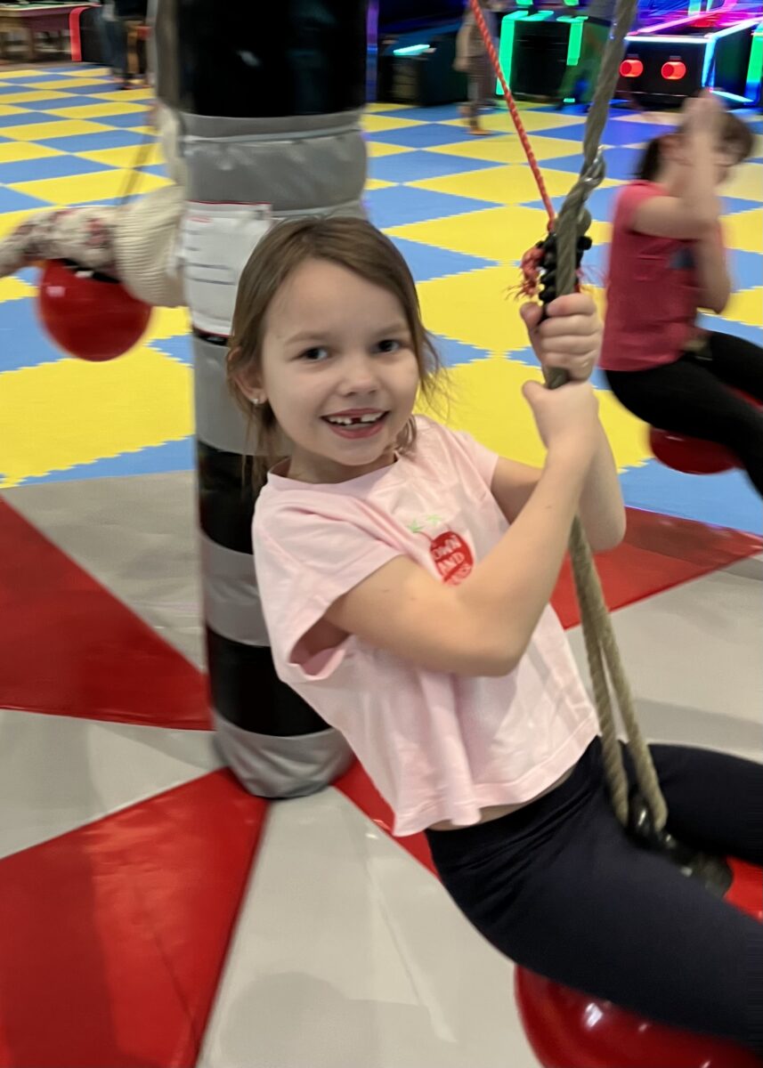 Maja z dużym uśmiechem się trzyma kulki która wisi i rusza się w okół punktu