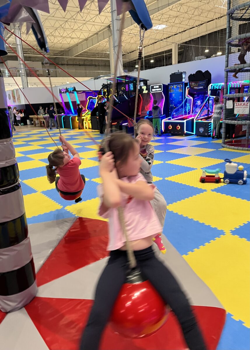 dziewczyny z uśmiechem się trzymają kulki która wisi i rusza się w okół punktu, tak szybko się kręci, że Maja jest rozmazana z przodu